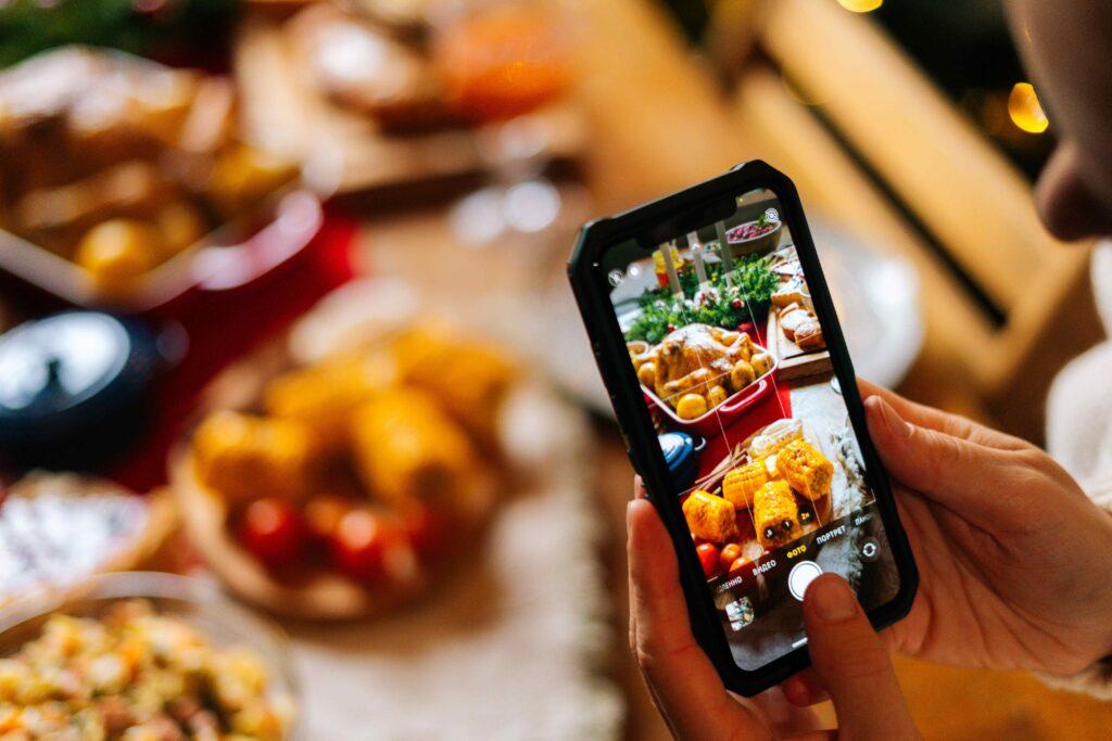 Nahaufnahme einer nicht wiederzuerkennenden jungen Frau, die mit ihrem Mobiltelefon ein Foto oder Video von einem schönen Weihnachtstisch macht. Bloggerin fotografiert Essen beim Weihnachtsessen.